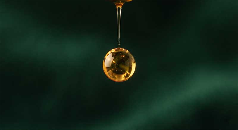 Golden liquid droplet suspended against a dark green background, representing colostrum