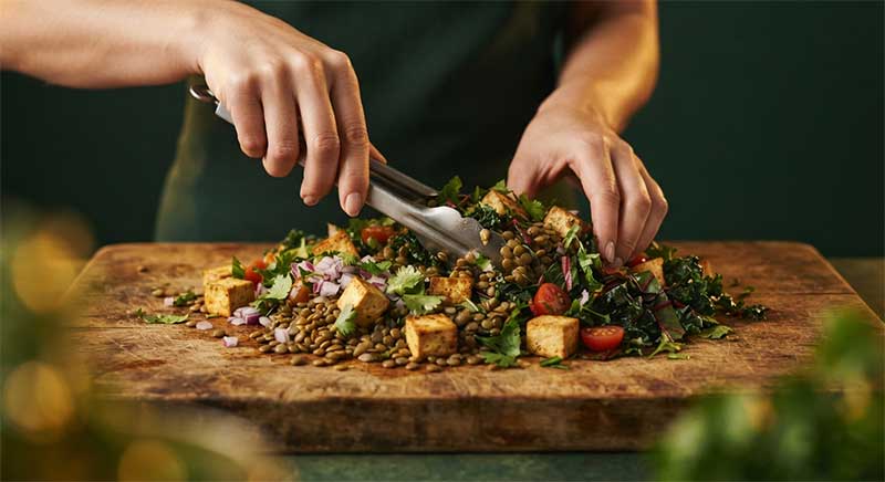 A parent's hands preparing a colorful plant-based meal with lentils, tofu, and greens